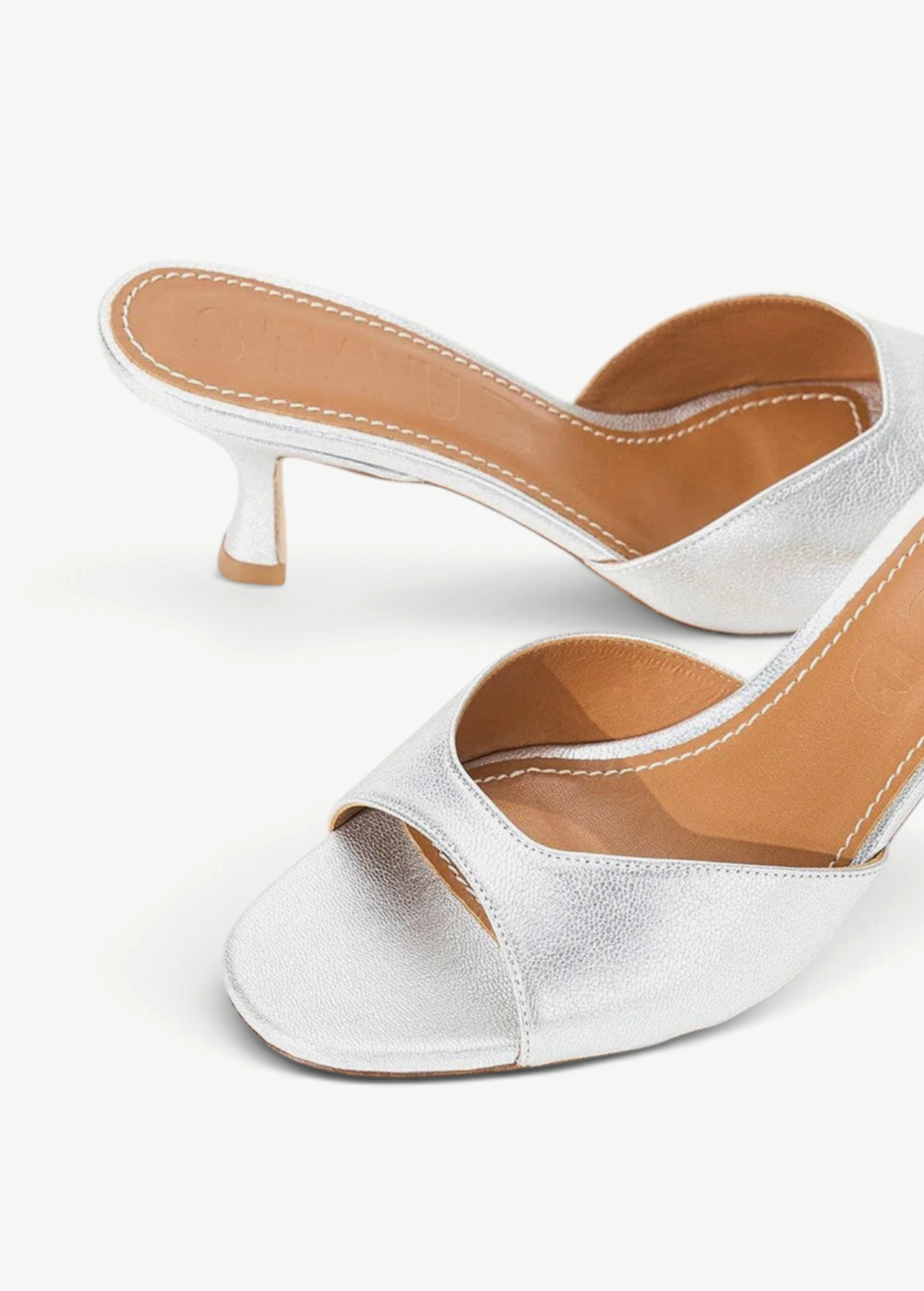 Brigitte Heel silver metallic kitten-heel mules with an open toe and tan leather footbed, featuring a refined silhouette.