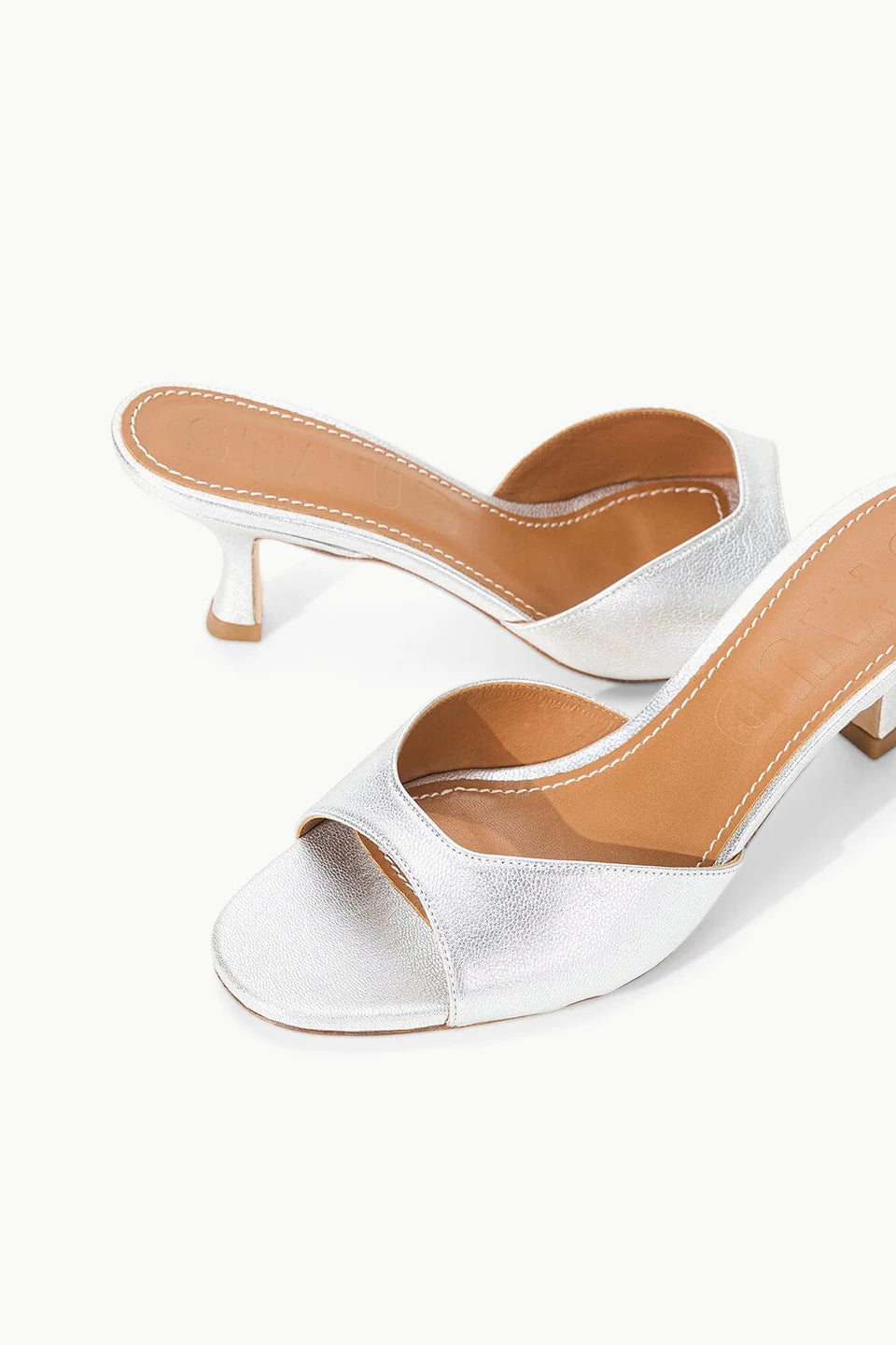 Brigitte Heel silver metallic kitten-heel mules with an open toe and tan leather footbed, featuring a refined silhouette.