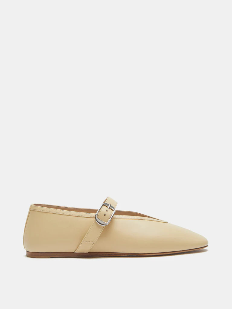 A pair of Stella Slipper Leather Shoes in custard leather, designed in a beige hue with a flat sole, pointed toe, and an elegant buckle. A single silver strap crosses the instep, displayed on a white background.