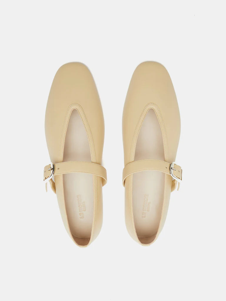 Beige Stella Slipper Leather Shoes, crafted from soft custard leather with square toes and an elegant buckle on the straps, are shown from above on a white background. These shoes offer timeless charm and refined detail.