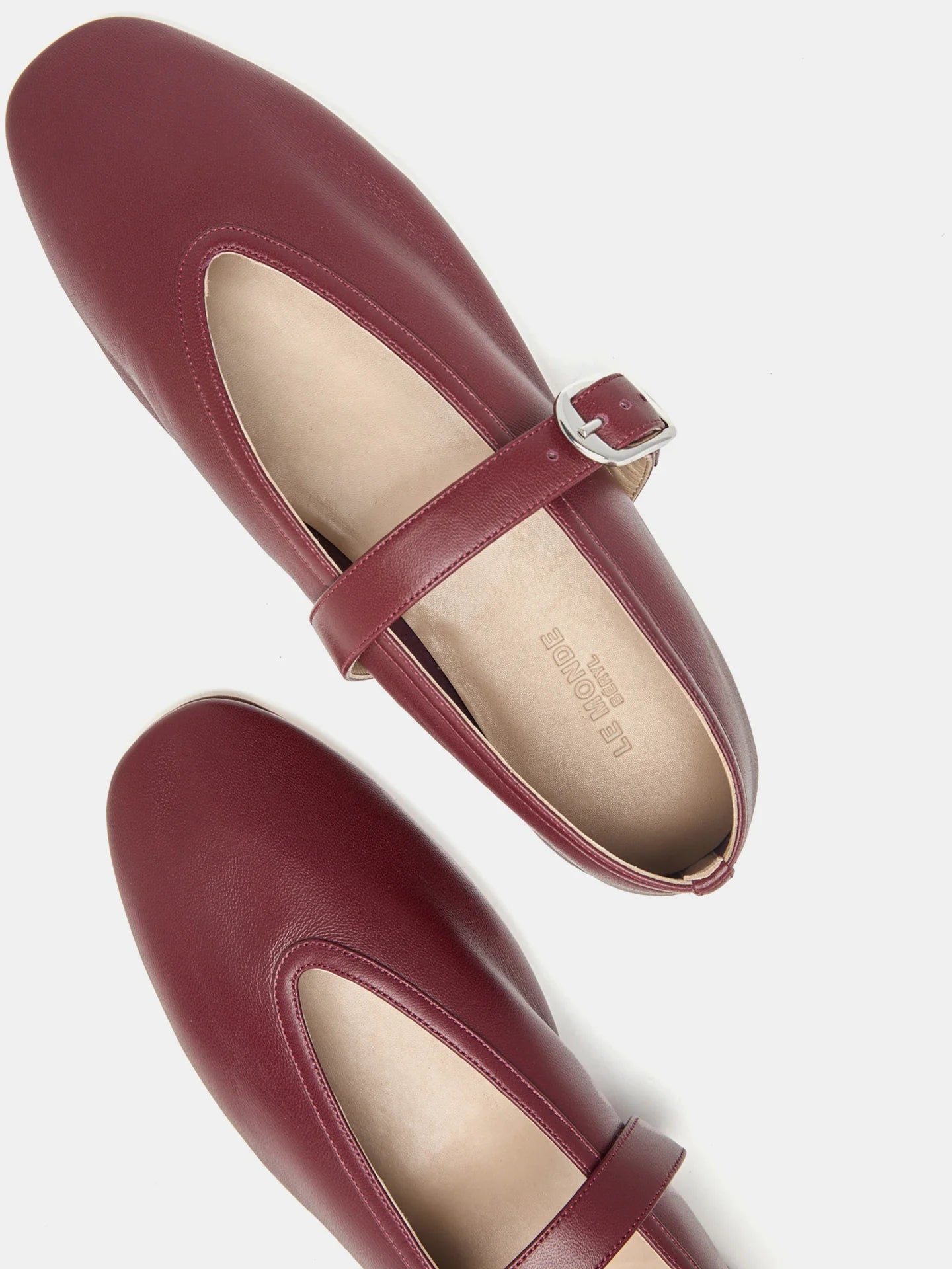 Top view of a pair of maroon Stella Slipper Leather Shoes crafted from rouge leather, featuring a polished buckle strap and beige insoles, displayed on a white background.