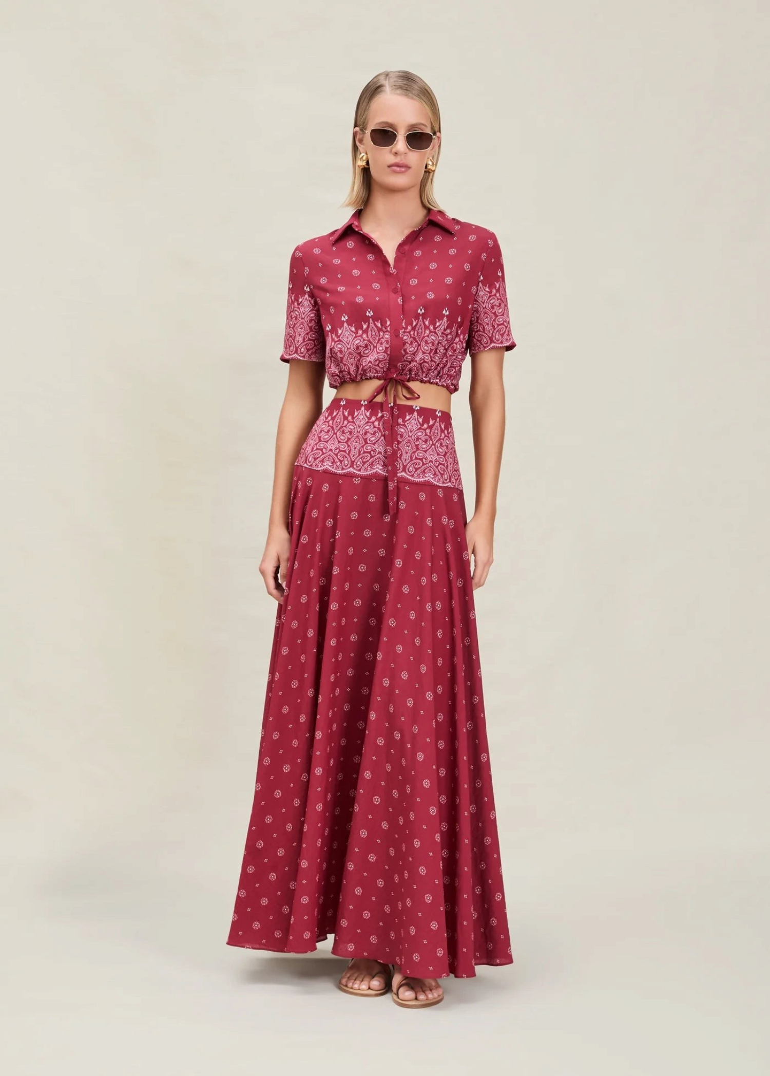 A model wearing a Rosie Top, a cropped, short-sleeved button-down shirt, paired with a matching high-waisted maxi skirt in a deep red bandana print.