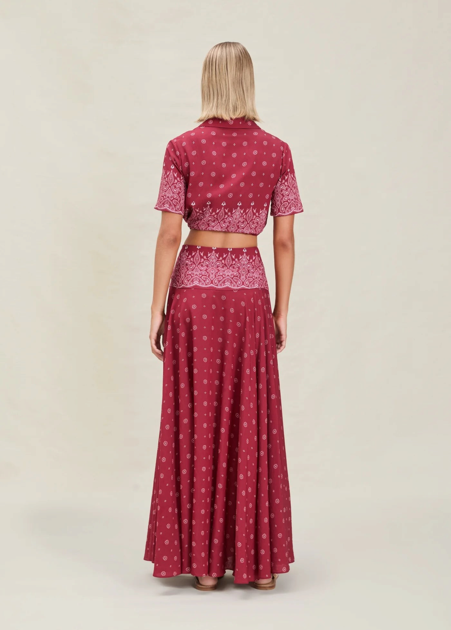 A person seen from behind wears a deep red Rosie Top with white bandana print, paired with a matching maxi skirt featuring a cropped, short-sleeved button-up design and an adjustable drawstring waist.