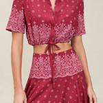 The Rosie Top is a cropped, short-sleeved collared shirt in a dark red paisley print with an adjustable drawstring waist and a tie front.