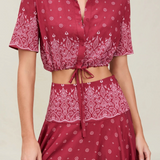 The Rosie Top is a cropped, short-sleeved collared shirt in a dark red paisley print with an adjustable drawstring waist and a tie front.