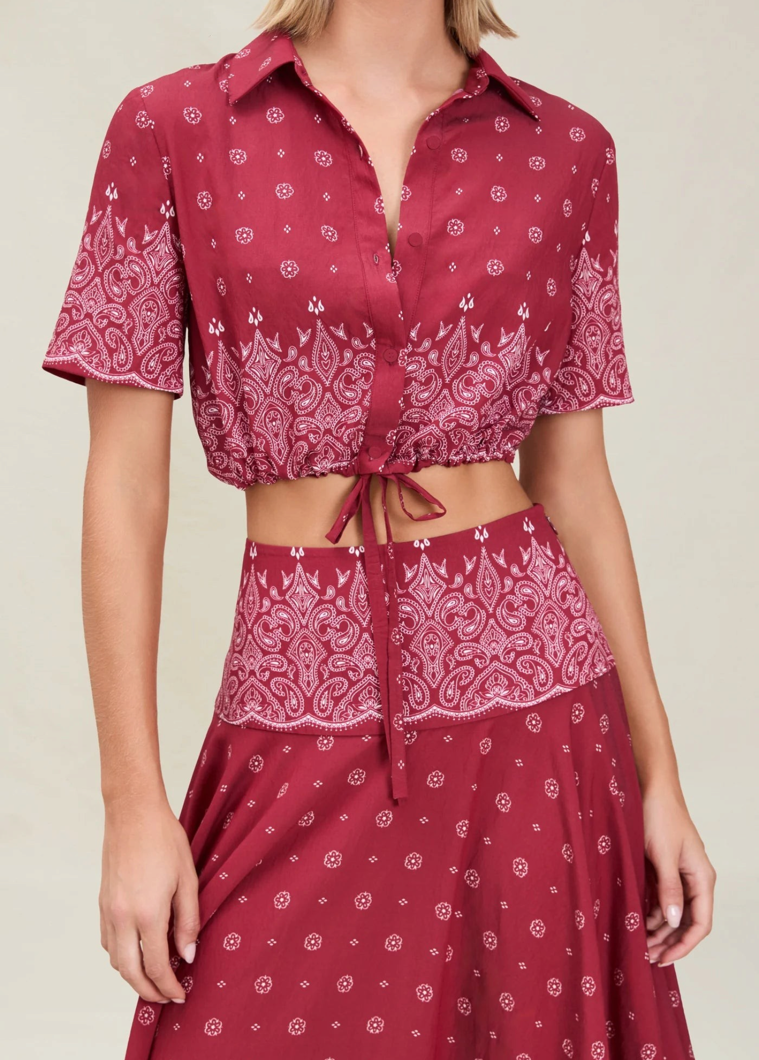 The Rosie Top is a cropped, short-sleeved collared shirt in a dark red paisley print with an adjustable drawstring waist and a tie front.