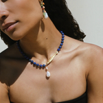 KABE SHOP INC Ospina necklace featuring blue lapis beads, a gold fish pendant, and a freshwater pearl on a model