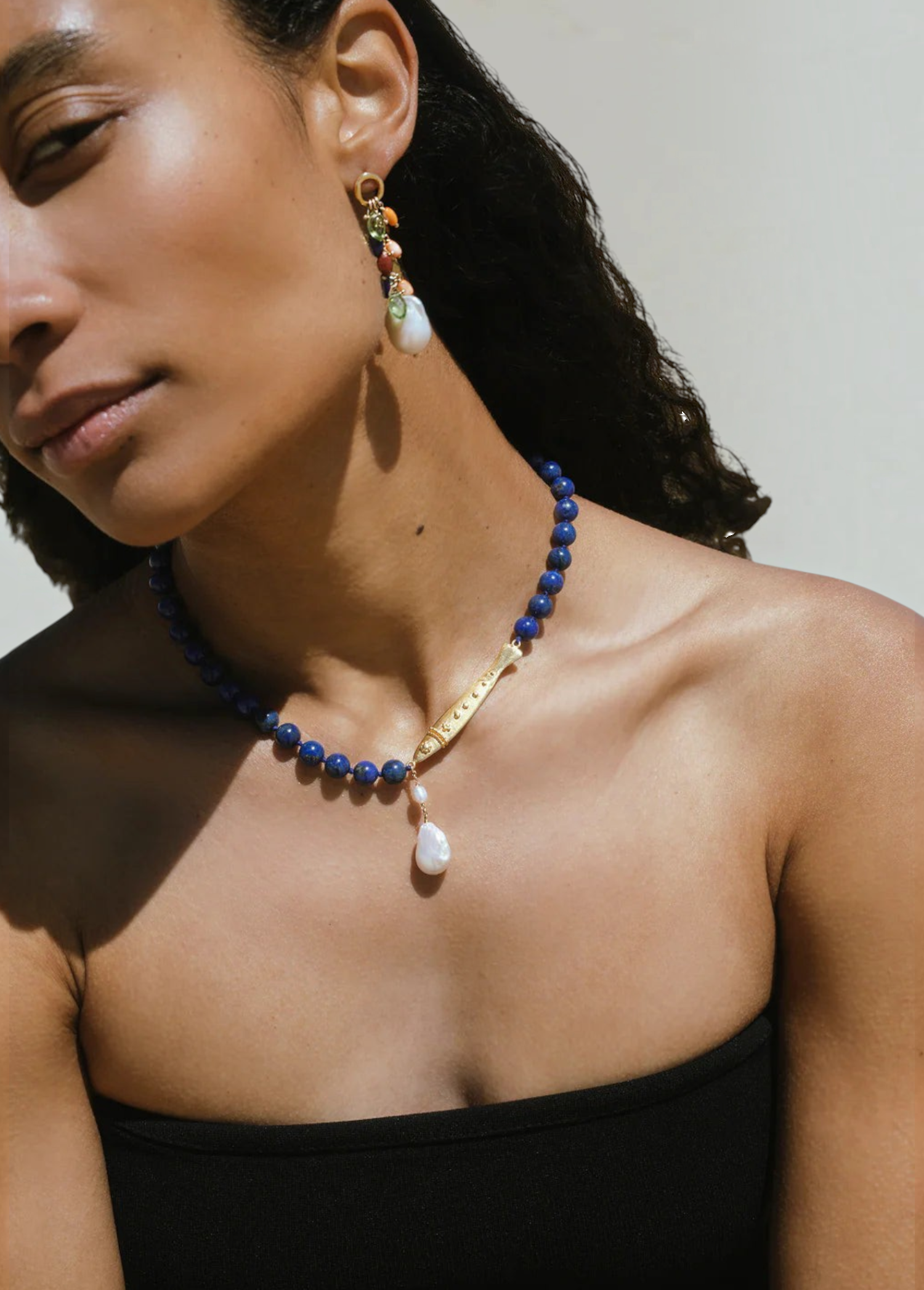 KABE SHOP INC Ospina necklace featuring blue lapis beads, a gold fish pendant, and a freshwater pearl on a model