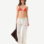 Woman wearing a red bikini top and white pants with colorful patterns on a white background