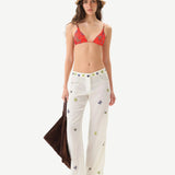 Woman wearing a red bikini top and white pants with colorful patterns on a white background