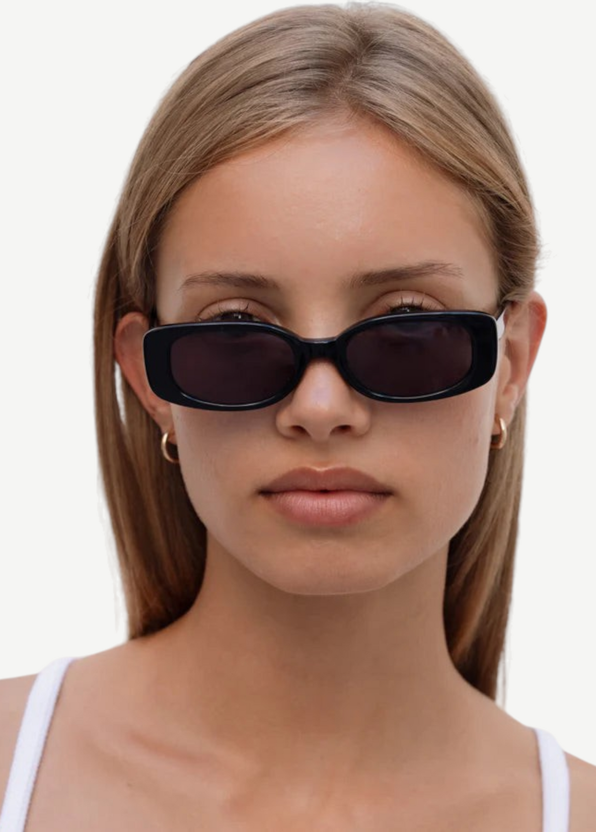 A woman with straight, light brown hair wears the Solene slim rectangle sunglasses in black, which provide 100% UV protection, paired with gold hoop earrings. She is looking straight ahead with a neutral expression and dressed in a white top against a plain background.