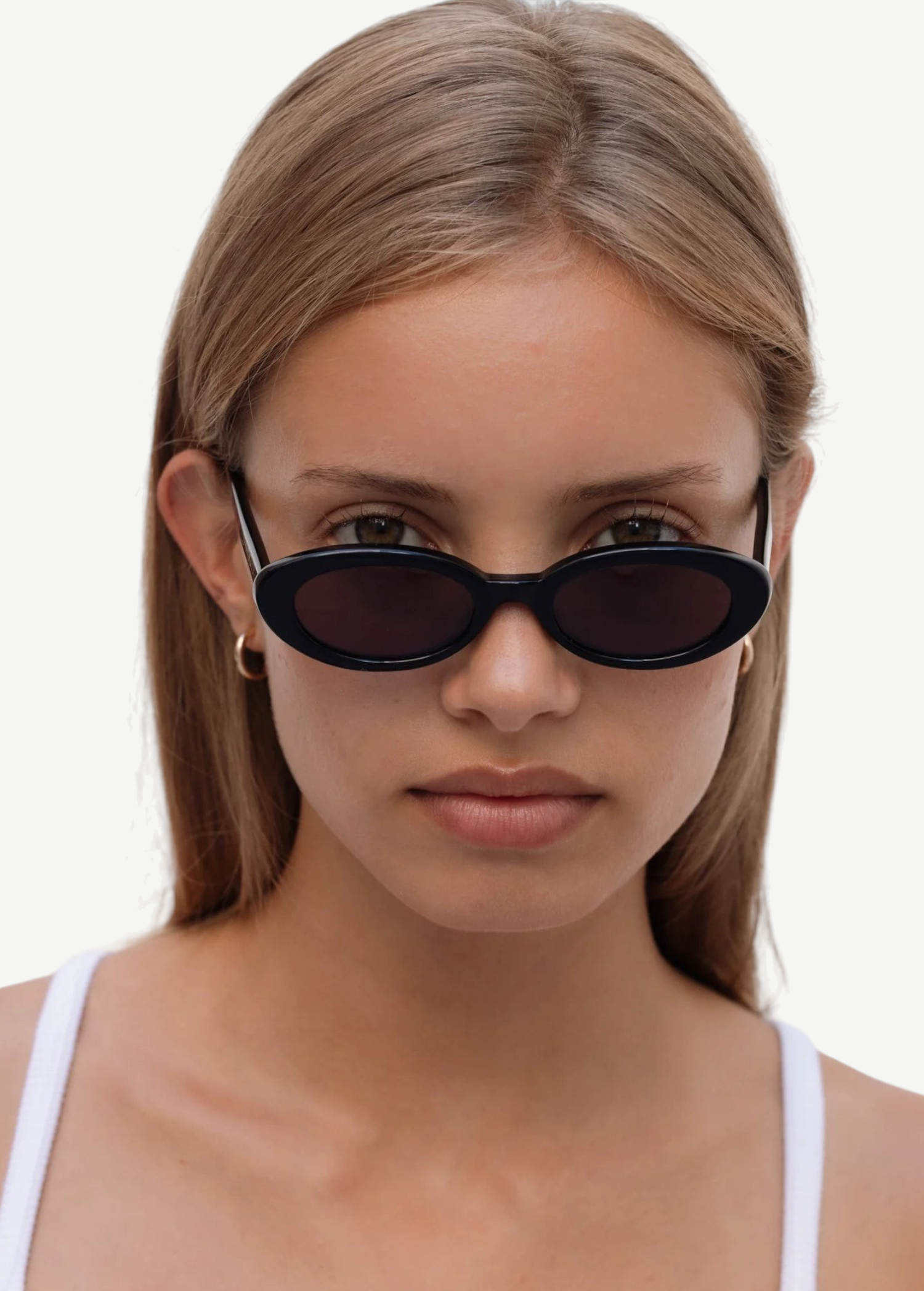 A young woman with straight light brown hair wears the Sylvie sunglasses in classic black and a white tank top, looking directly at the camera against a plain white background.