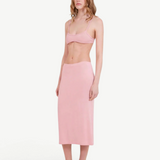 A woman stands against a plain light background, wearing a light pink bralette and the Tube Skirt crafted from soft bamboo fabric, paired with black slip-on shoes. Her hair is loose, and she has a neutral expression, highlighting the minimalist design of her outfit.