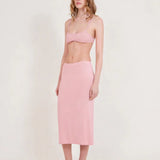 A woman stands against a plain light background, wearing a light pink bralette and the Tube Skirt crafted from soft bamboo fabric, paired with black slip-on shoes. Her hair is loose, and she has a neutral expression, highlighting the minimalist design of her outfit.