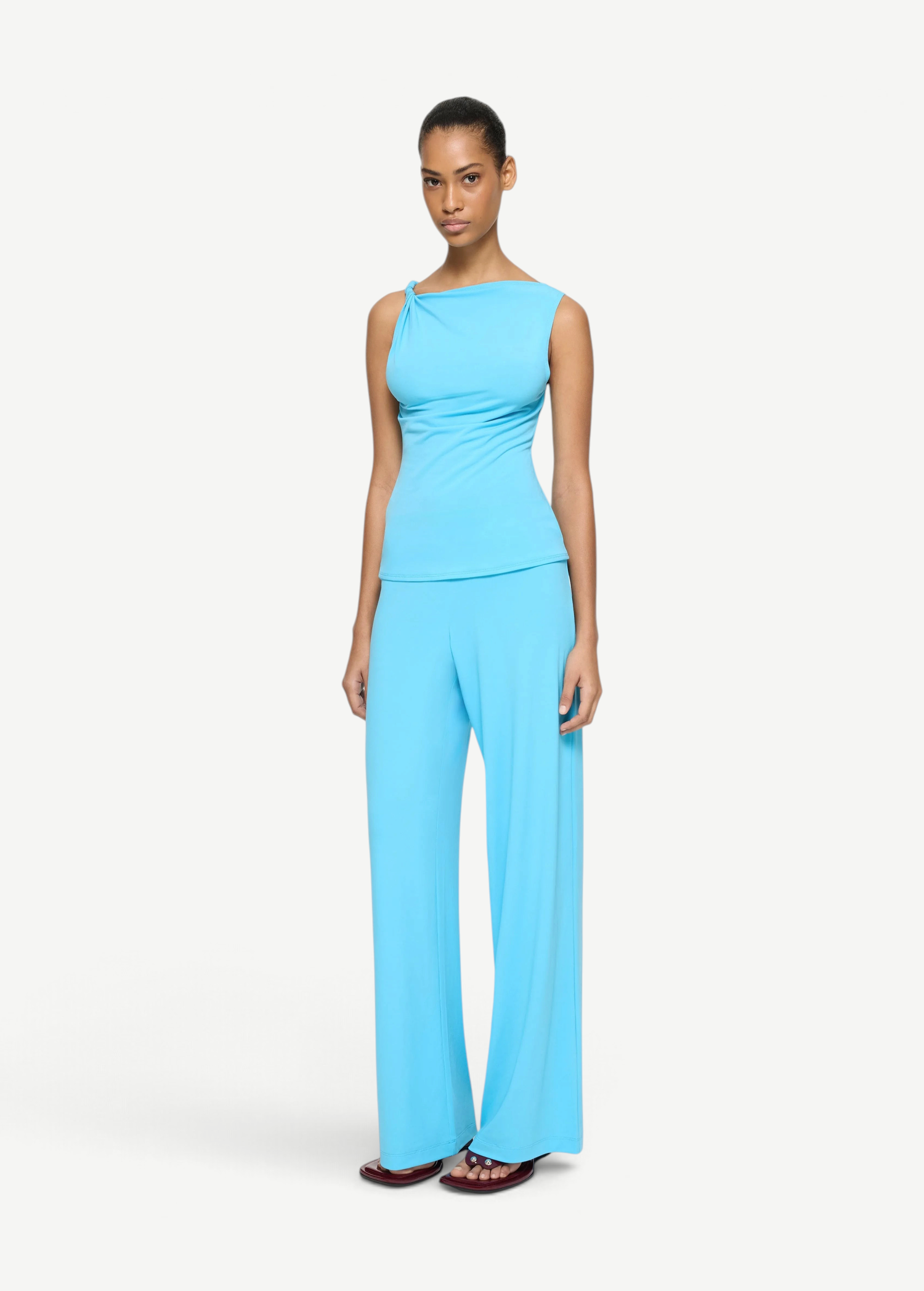 A person wears a bright blue Elemental Twist Singlet with an asymmetrical drape at the shoulder, paired with matching wide-leg pants.