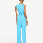 A person seen from behind, wearing an Elemental Twist Singlet in a bright blue with a sculptural shoulder and matching wide-leg trousers.
