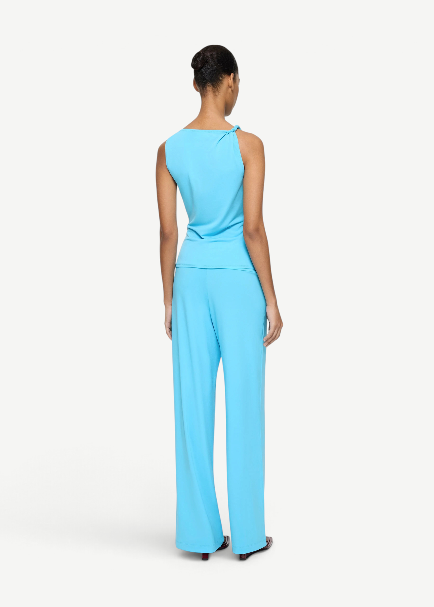 A person seen from behind, wearing an Elemental Twist Singlet in a bright blue with a sculptural shoulder and matching wide-leg trousers.