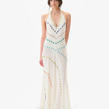 A person stands against a plain white background wearing the Vicka Dress—a sleeveless, floor-length white backless dress embellished with colorful circular beads arranged in curved lines, featuring intricate bead embroidery and a subtly flared hemline.