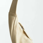 Close-up of the Vancouver Sling Bag, a beige sculptural shoulder bag crafted from supple nappa leather, featuring a curved strap and a visible seam, photographed against a plain white background.