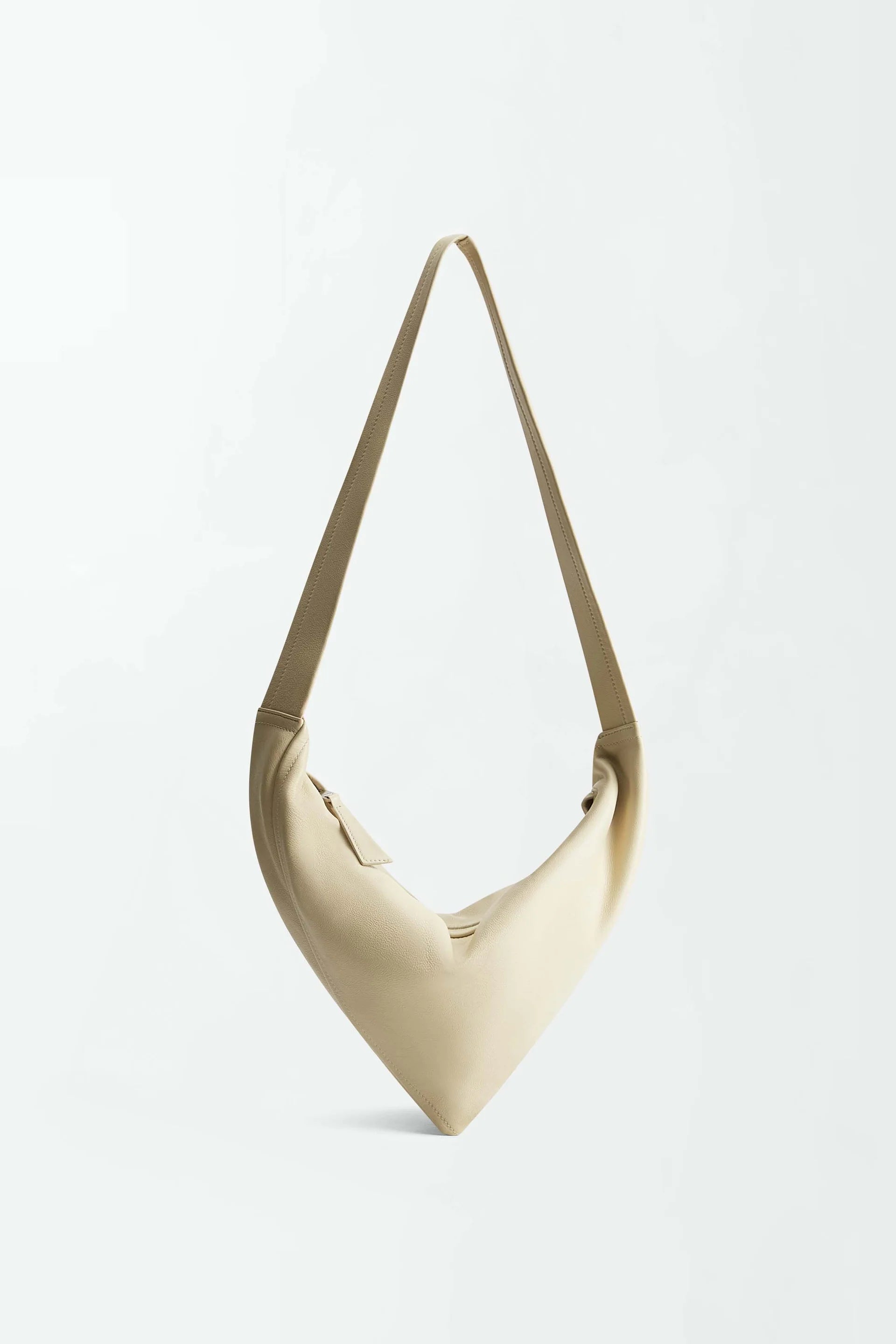 The Vancouver Sling Bag, shown against a plain white background, is a beige, triangular-shaped sculptural shoulder bag crafted from supple nappa leather and features a single strap.