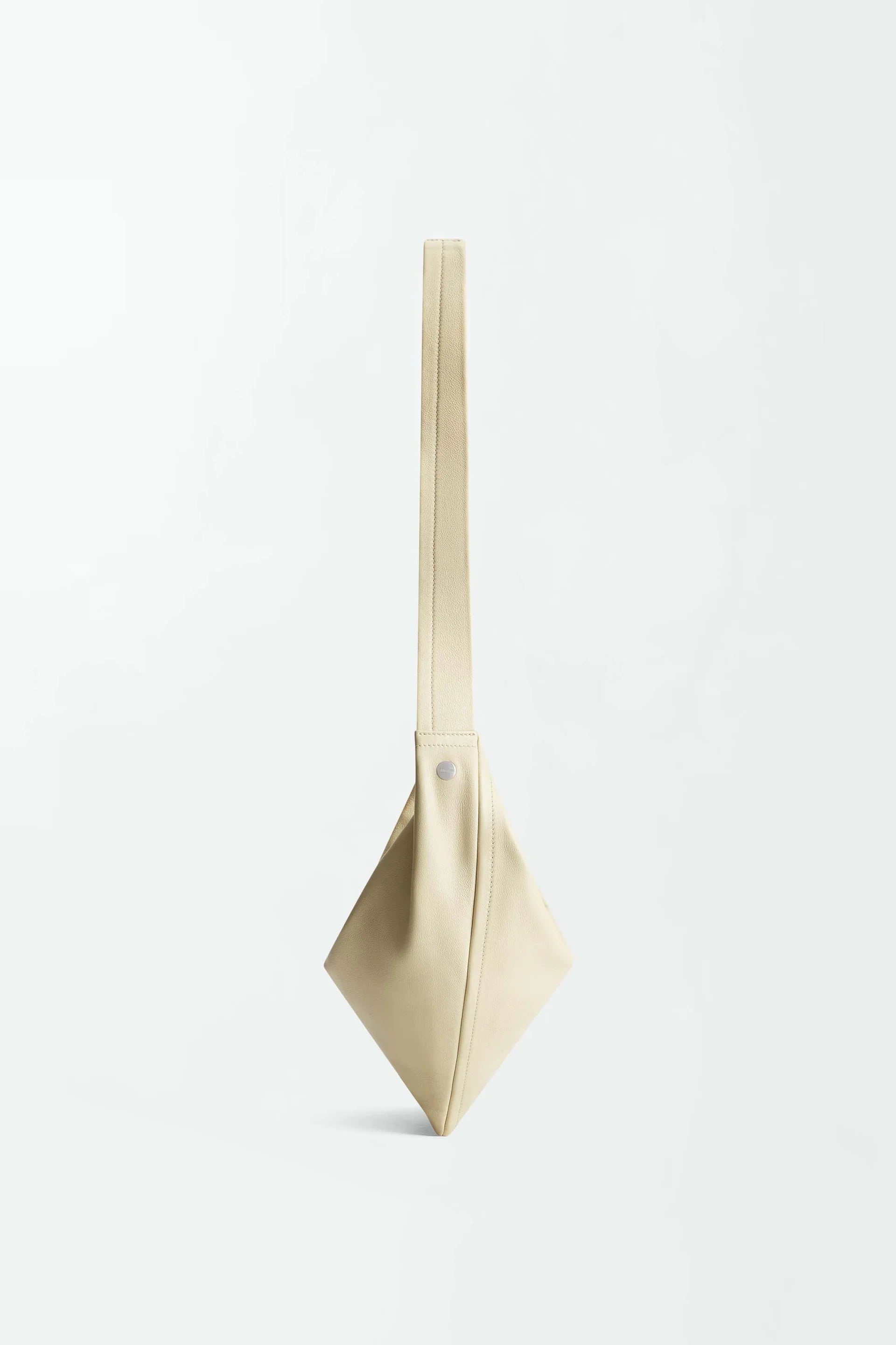 The Vancouver Sling Bag, crafted from supple nappa leather in beige, is displayed against a plain white background. Its geometric sculptural shape features clean lines, a minimalist design, and a single wide strap.