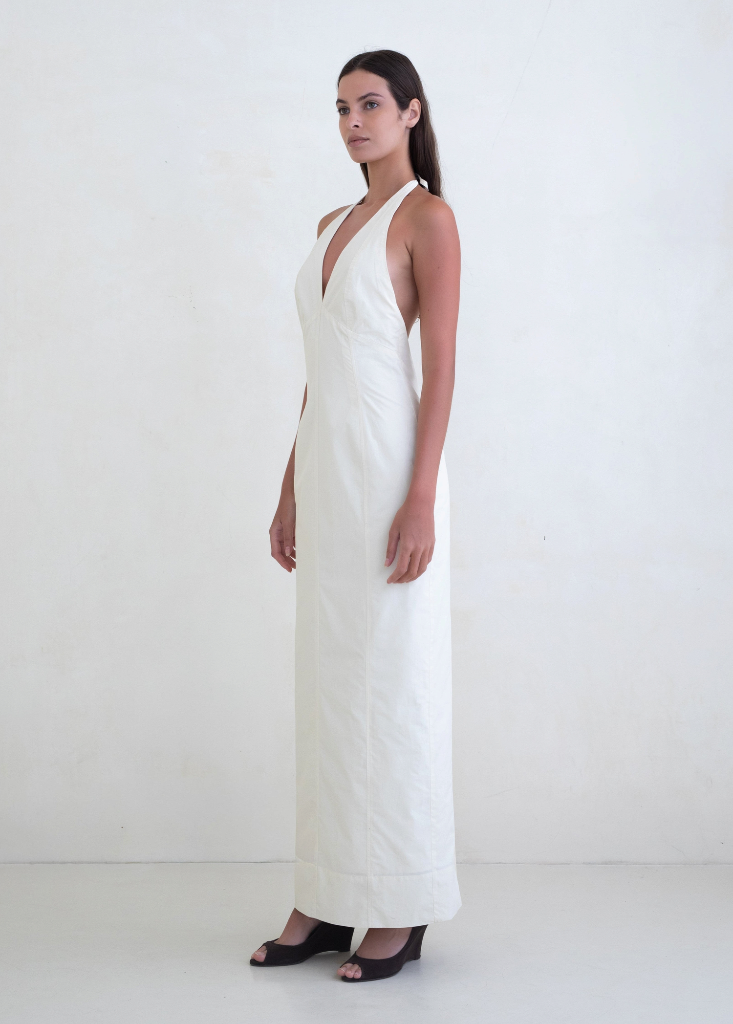Model wearing a white KABE SHOP INC Helia halter gown with a plunging neckline and floor-length silhouette