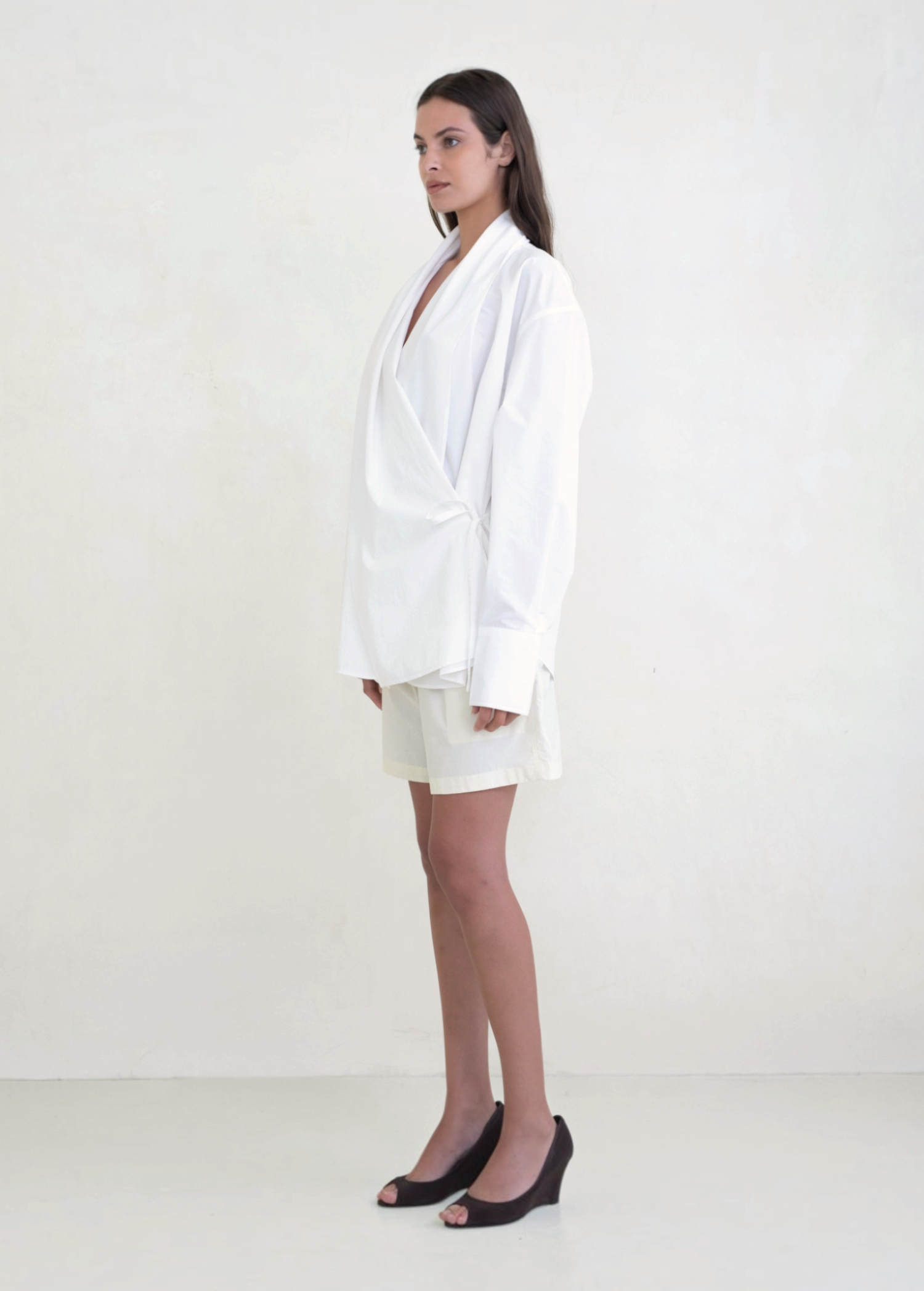 Model wearing a white KABE SHOP INC Leandra wrap shirt with long sleeves and a relaxed silhouette, side view.