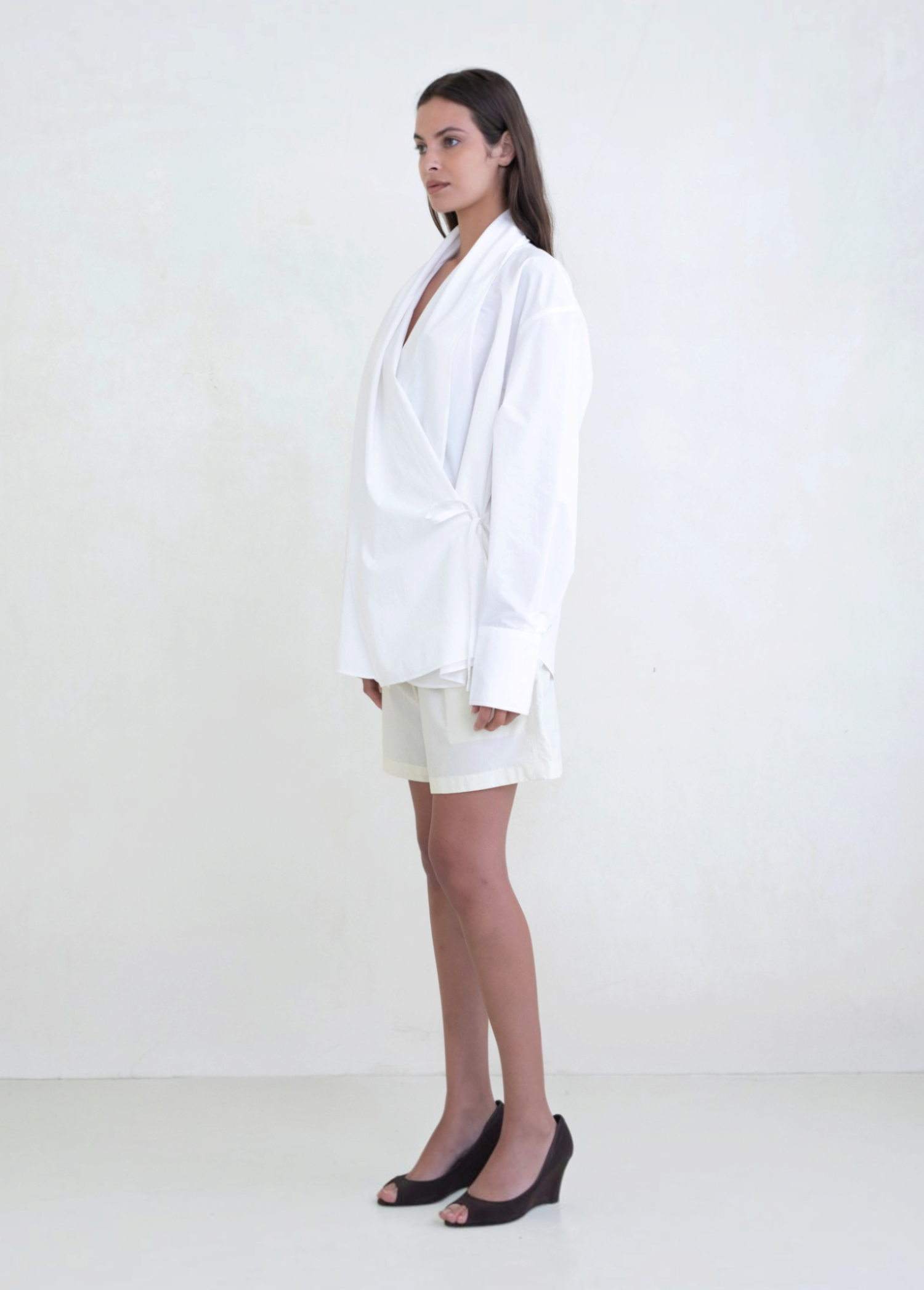 Model wearing a white KABE SHOP INC Leandra wrap shirt with long sleeves and a relaxed silhouette, side view.