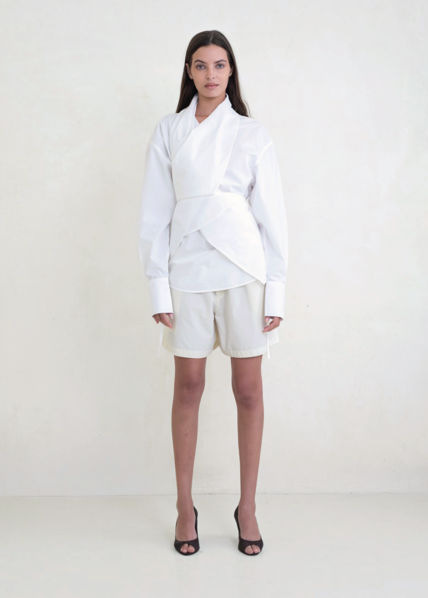 Model wearing KABE SHOP INC Leandra white convertible wrap shirt with long sleeves and tailored shorts
