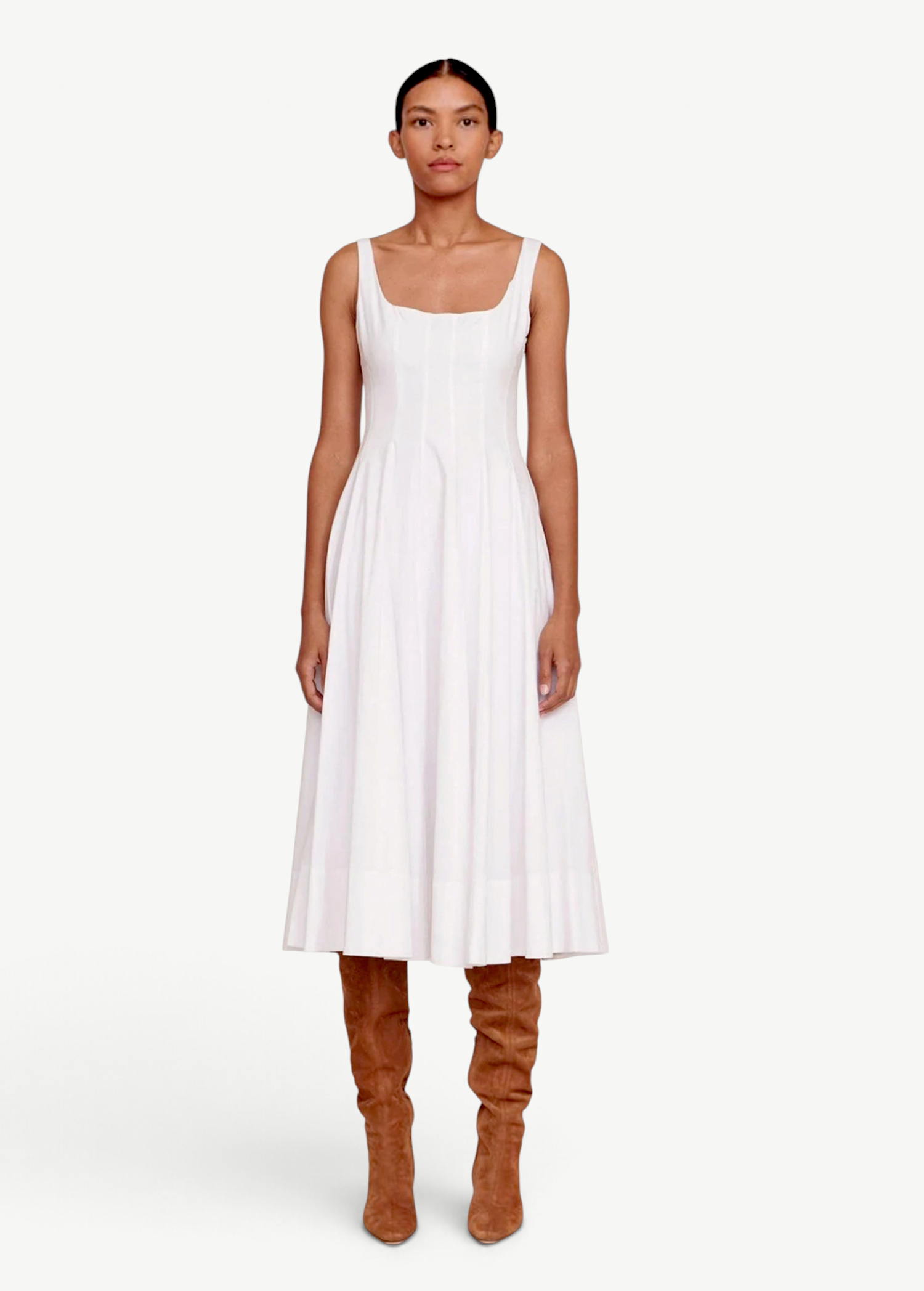 Model wearing a white KABE SHOP INC Wells midi dress with a square neckline and pleated skirt, paired with brown boots.
