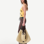 Model wearing KABE SHOP INC Flo pants with lace-up waist and lettuce-edge hem, paired with a large straw tote bag.