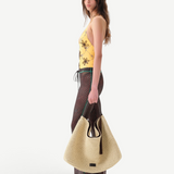 Model wearing KABE SHOP INC Flo pants with lace-up waist and lettuce-edge hem, paired with a large straw tote bag.