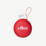 A round, red zippered case with “ellaz” printed in white letters houses Reusable Nippz nipple covers. A small attached tag reads “NIPPS, REUTILIZABLES, CREMA NUDE.” The case features a red wrist strap and is displayed against a plain white background.