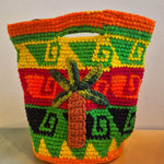 Introducing the Palmeras Bag Sac: a handmade crocheted wool bucket bag adorned with vivid geometric patterns in orange, green, yellow, and red. The front showcases a raised palm tree design, while the interior features a playful leopard lining. Set against a neutral background, this one-of-a-kind accessory energizes any setting with its vibrant style.
