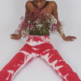 A person sits on the floor wearing vintage-style red and white Tie Dye Jeans, holding a bouquet of small pink and white flowers against their chest.