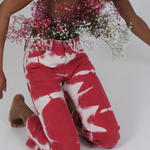 A person kneeling, wearing reworked vintage Tie Dye Jeans in red and white with a bouquet of baby’s breath tucked into the waistband.