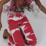 A person kneeling, wearing reworked vintage Tie Dye Jeans in red and white with a bouquet of baby’s breath tucked into the waistband.