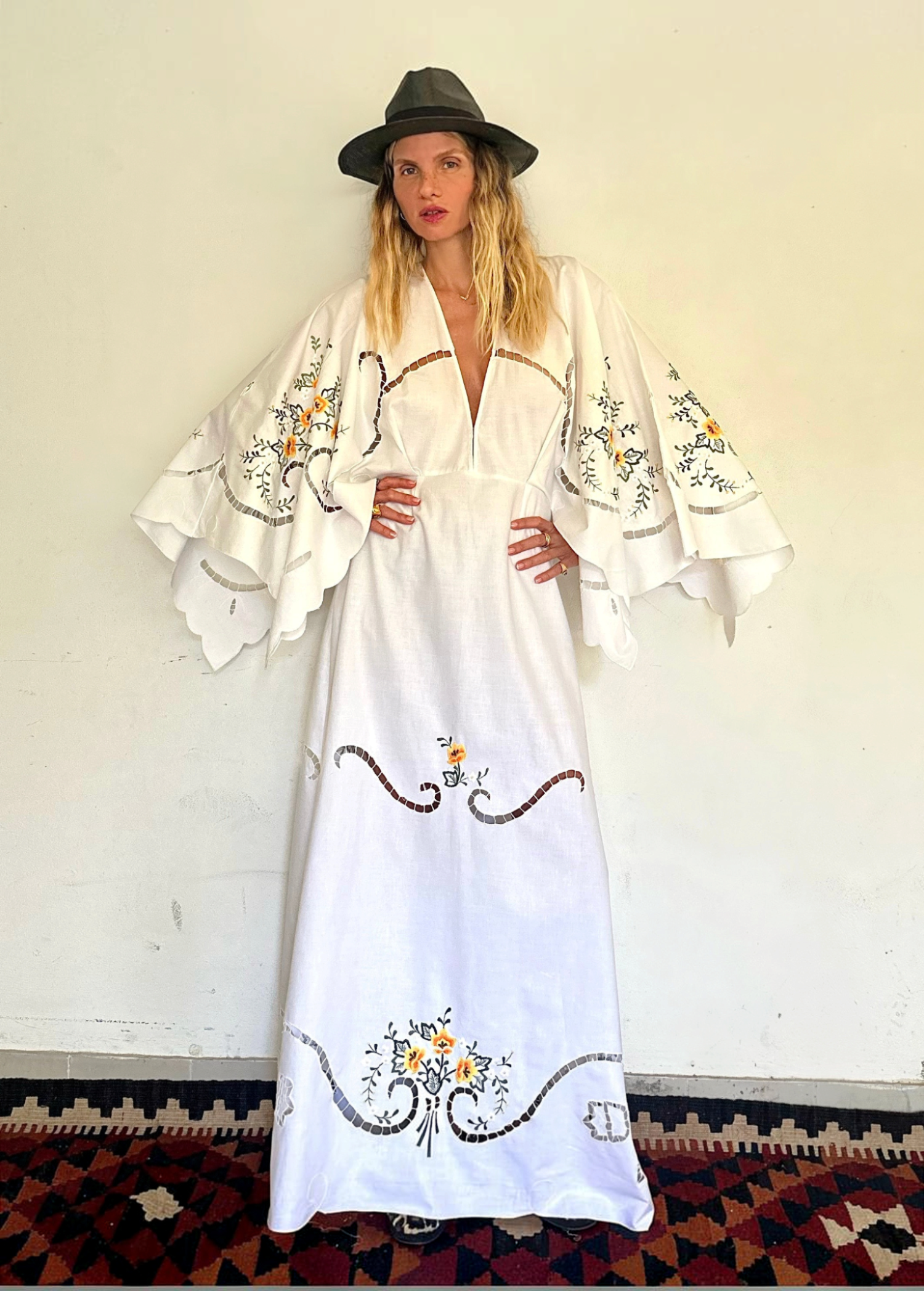 KABE SHOP INC white maxi dress with wide sleeves, floral embroidery, and cut-out details worn by a model in a hat.