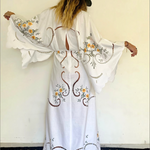 KABE SHOP INC white maxi dress with wide sleeves, floral embroidery, and cut-out details worn with a black hat.