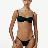 Model wearing KABE SHOP INC Copa Bottom, a black micro-cut bikini bottom with high-cut legs and slim side straps.