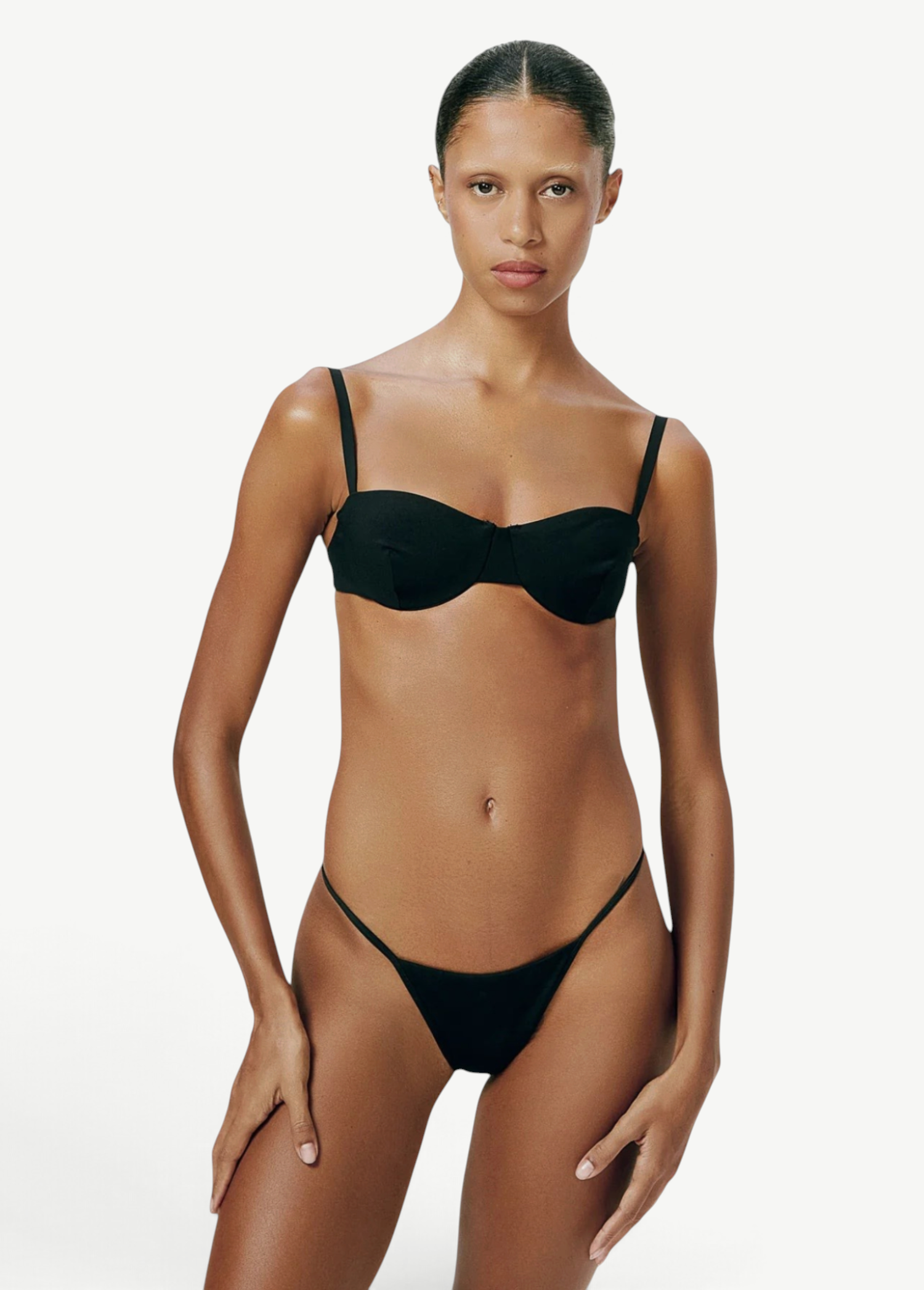 Model wearing KABE SHOP INC Copa Bottom, a black micro-cut bikini bottom with high-cut legs and slim side straps.