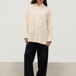 A person wears a pale yellow Shea Embroidered Hemp Blend Shirt with geometric floral embroidery along the placket, paired with wide-leg black trousers and black sandals.