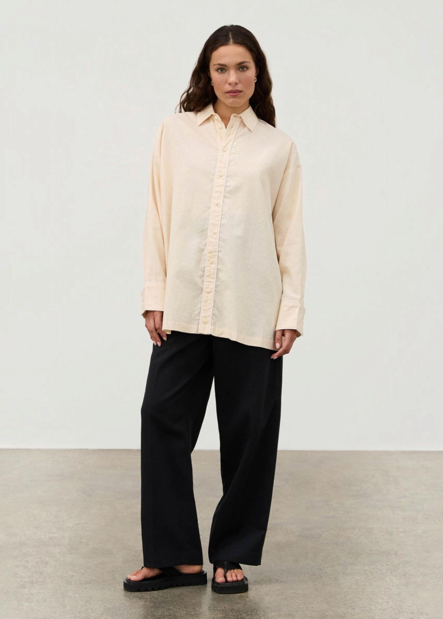 A person wears a pale yellow Shea Embroidered Hemp Blend Shirt with geometric floral embroidery along the placket, paired with wide-leg black trousers and black sandals.