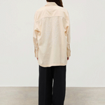 A person seen from behind wears the Shea Embroidered Hemp Blend Shirt, a long-sleeved, light-colored top with white geometric floral embroidery on the back, paired with loose black trousers.
