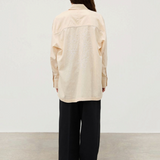 A person seen from behind wears the Shea Embroidered Hemp Blend Shirt, a long-sleeved, light-colored top with white geometric floral embroidery on the back, paired with loose black trousers.