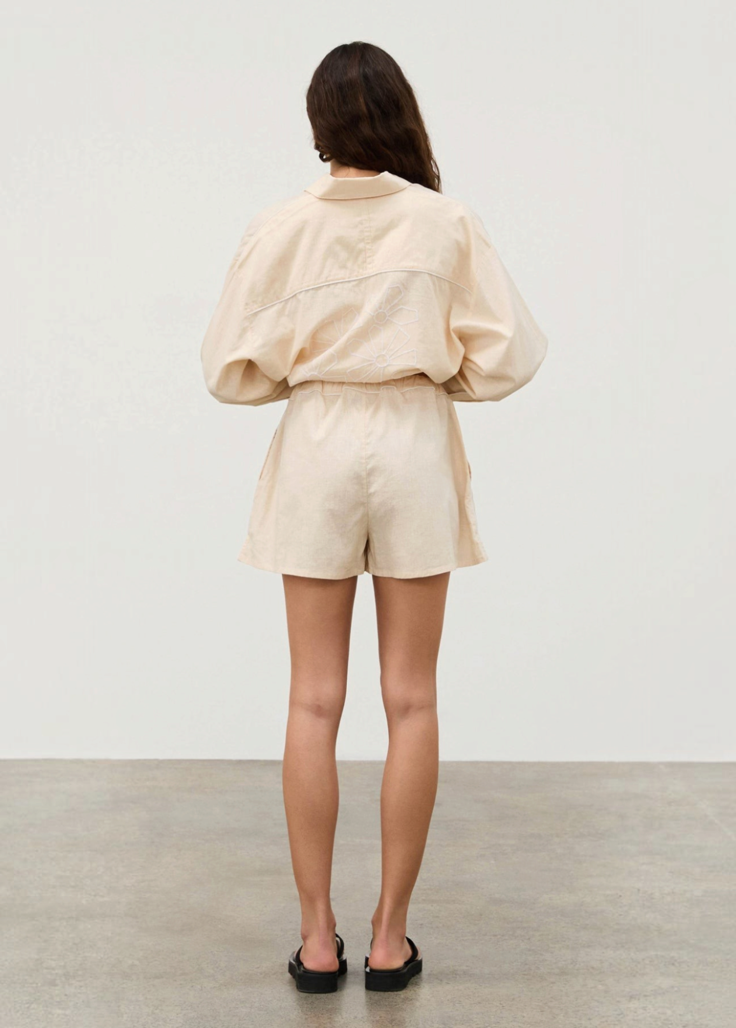 Back view of a person wearing a Shea Embroidered Hemp Blend Shirt in light beige with white geometric floral embroidery, paired with matching shorts.