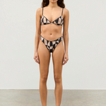 Model wearing KABE SHOP INC Mosaic Curve thong bikini with hand-painted geometric print and black piping details.