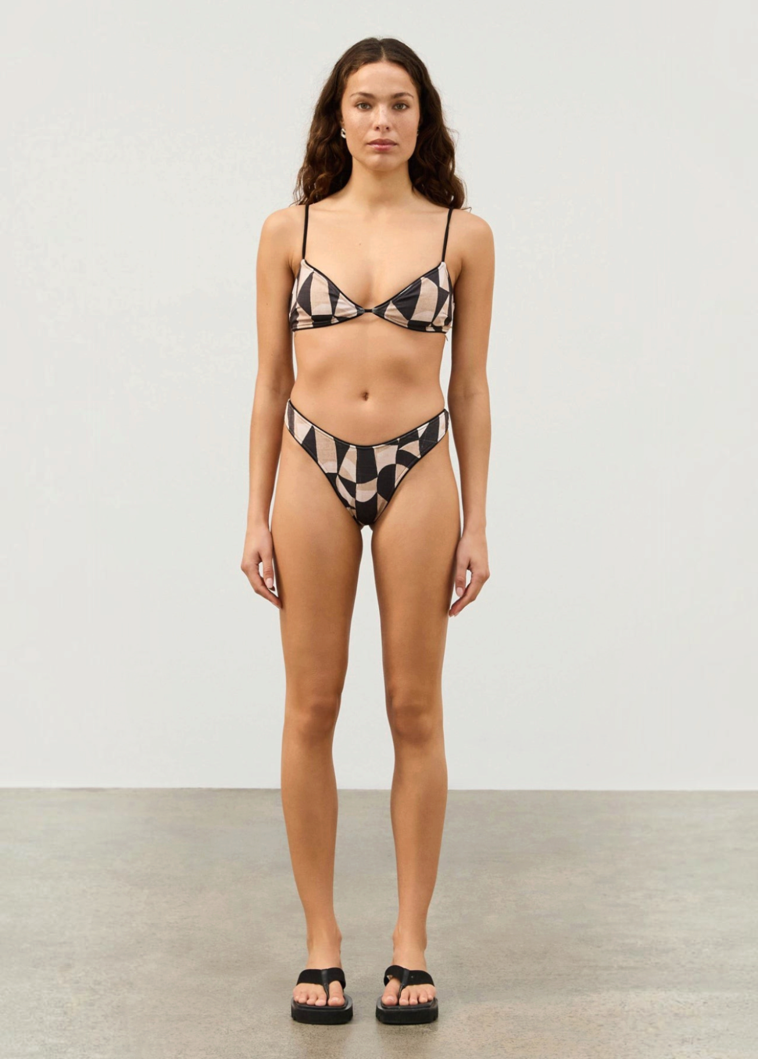Model wearing KABE SHOP INC Mosaic Curve thong bikini with hand-painted geometric print and black piping details.