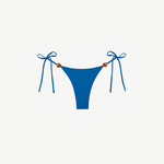 Praia Bottom in blue, crafted from eco-friendly Peach Perfect fabric, features adjustable side tie strings with brown bead accents on each hip. Displayed on a white background, this swimwear combines comfort and style for a flawless fit.