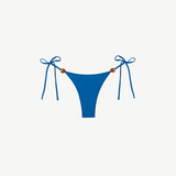Praia Bottom in blue, crafted from eco-friendly Peach Perfect fabric, features adjustable side tie strings with brown bead accents on each hip. Displayed on a white background, this swimwear combines comfort and style for a flawless fit.